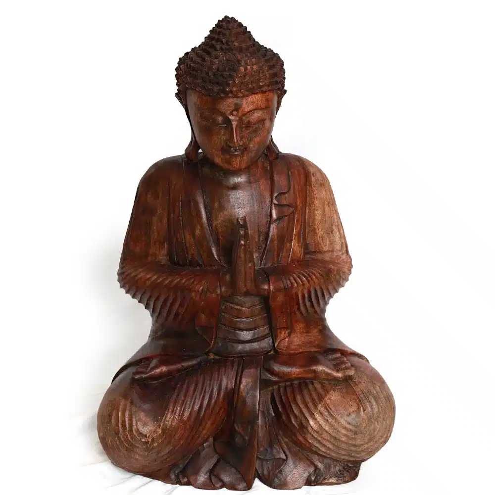 Eine hölzerne Buddha-Statue in sitzender Meditationshaltung, mit detailreich geschnitzter Robe und Kopfbedeckung, vor einem schlichten weißen Hintergrund. Die Hände sind in der Geste des Anjali Mudra (Gebetsgeste) zusammengelegt.